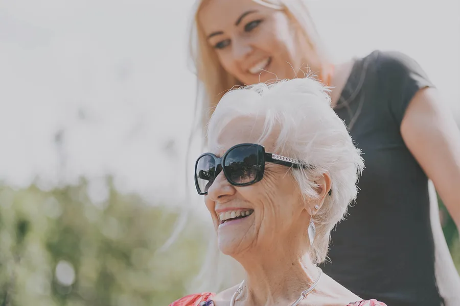 A smiling woman pushes an older lady in a wheelchair.