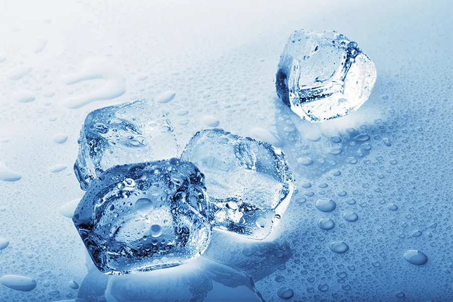 A close up shot of ice cubes on a blue surface. They are partially melted.