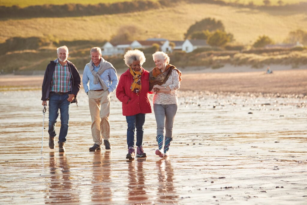 Group Of Smiling Senior Friends Walking Arm In Arm Along Shoreline Of Winter Beach