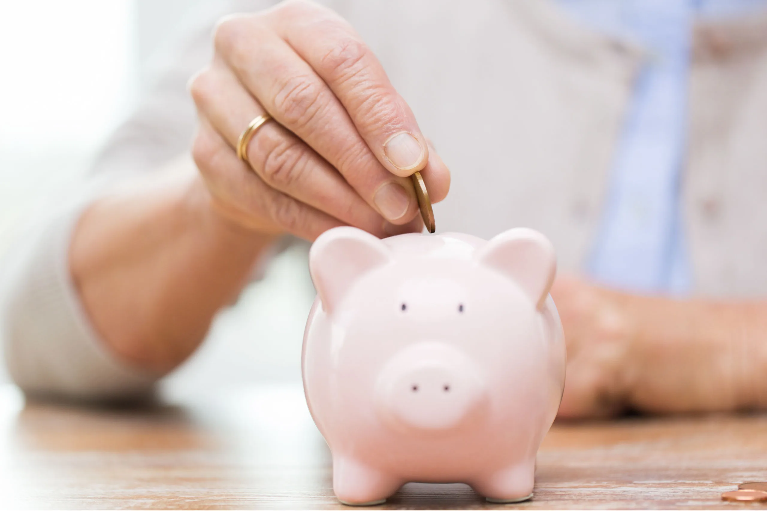 A small pink piggy bank, with a person's hand feeding a coin through the slot.