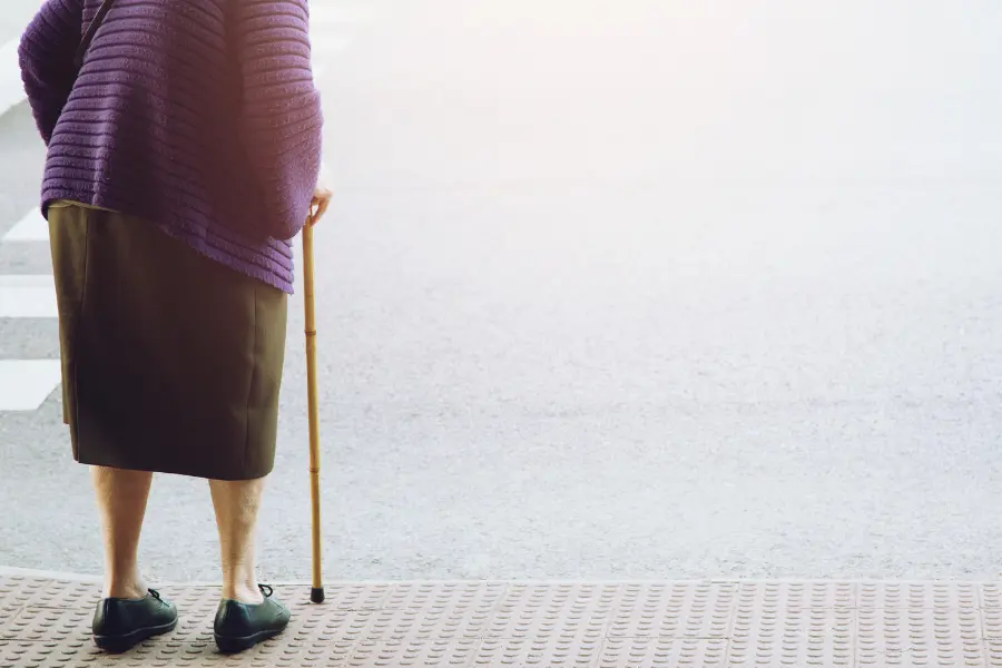 An older lady stood with her walking stick looking outside 