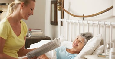 Adult Woman Reading Newspaper To Senior Woman