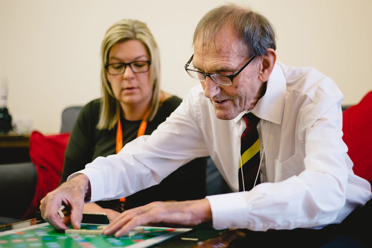 Elderly man playing scrabble with his Live In Care giver Unique Senior Care