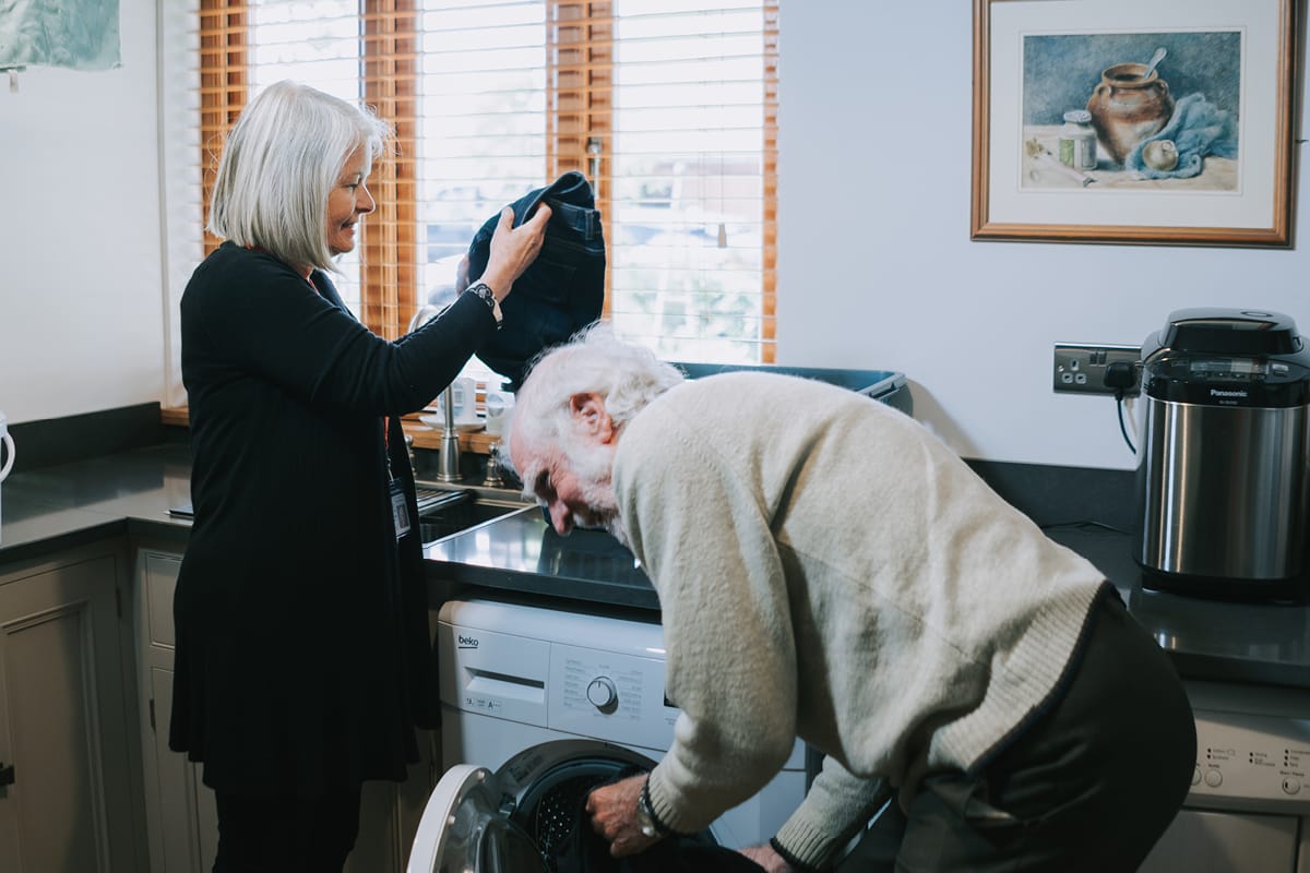 Elderly gentleman with live in carer next t washing machine for the section on what live in care costs include