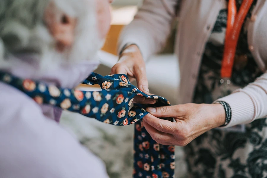 Caregiver assisting elderly gentleman with his tie in the types of live in care section Cheshire