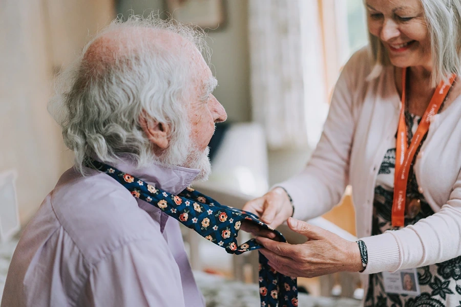 Unique carer assiting elderly male client with doing up his tie in the types of live in care service on the west midlands page