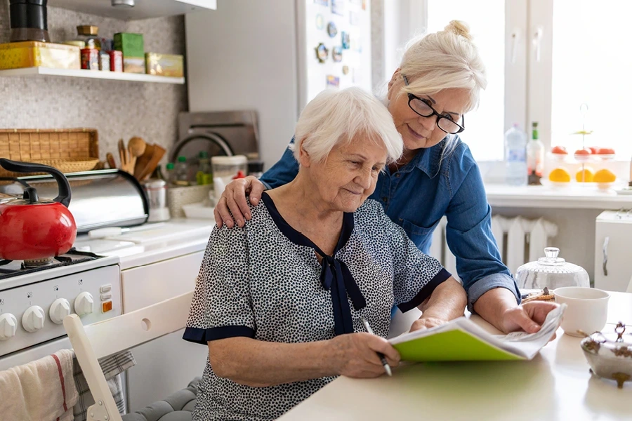 A carer with elderly lade client sat at a table looking over paperwork - in the why cost of live in care vary section of the West Midlands page