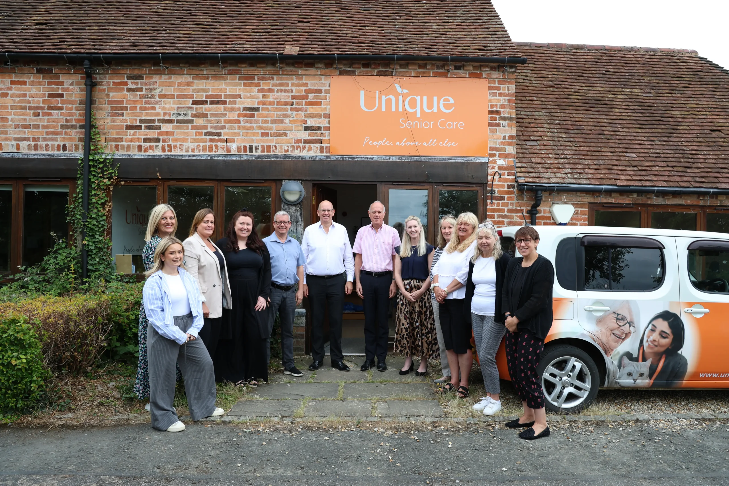 The Unique Senior Care head office team stood next to a branded Unique Senior Care car