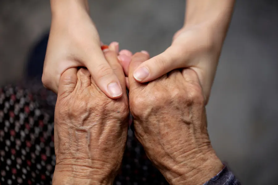 Close-up of two hands holding each other, one pair being elderly hands and the other pair being younger hands.