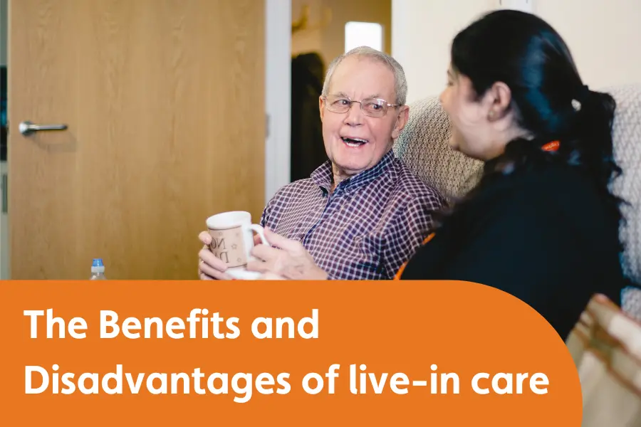 A gentleman and his carer sat smiling while chatting over a cup of tea