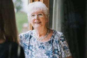 A lady stood by a window smiling at her carer