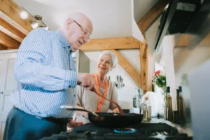 A gentleman and his carer smiling while cooking together