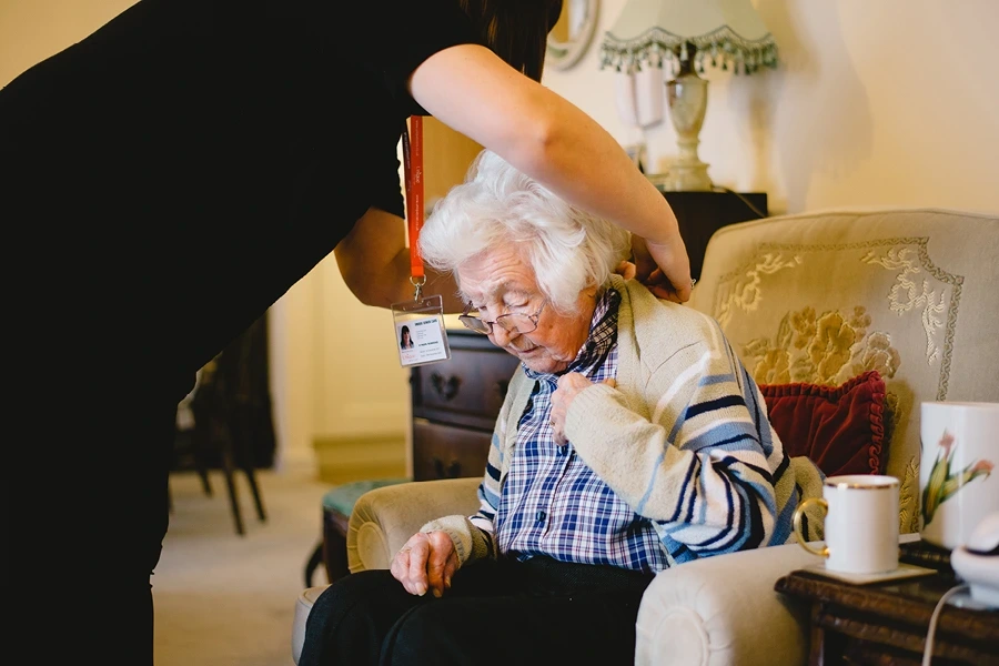 In the Ensuring Compatibility in Salop Live-in Care section, an image shows a caregiver assisting an elderly woman by putting a cardigan on her, highlighting the importance of matching caregivers to clients.