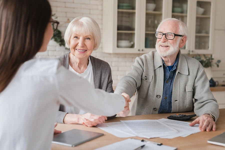 Older couple sat with care manager with man shaking hands with her across the table and displayed in the Kent Live in care page - questions to ask section