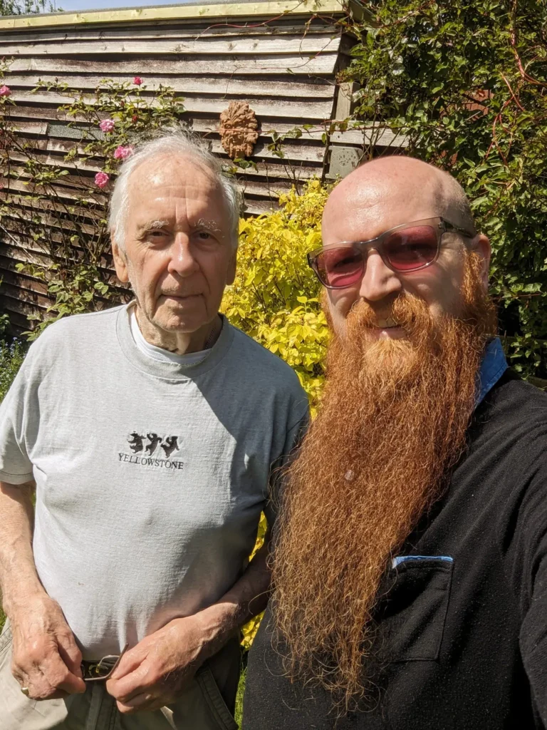 Philip Maultby, sottd outside in the sun with his carer Chris, both smiling