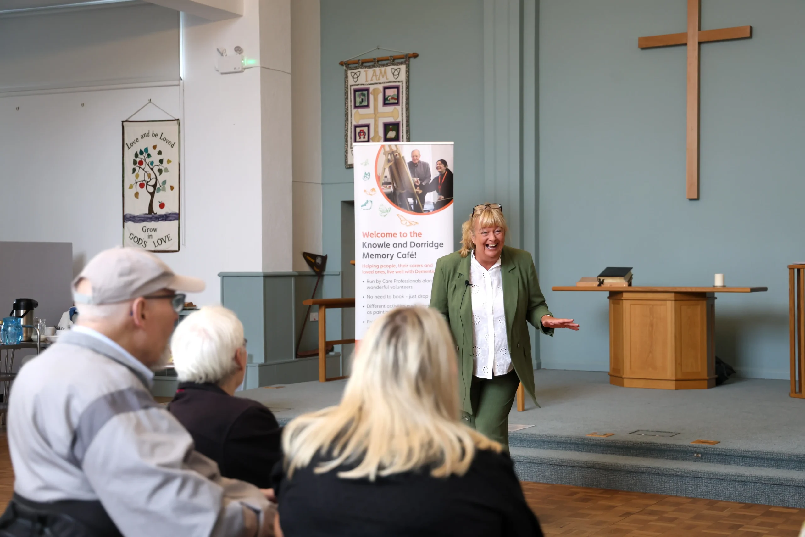 Jayne Vale speaking to attendees at the Family Dementia Workshop, with a banner in the background.