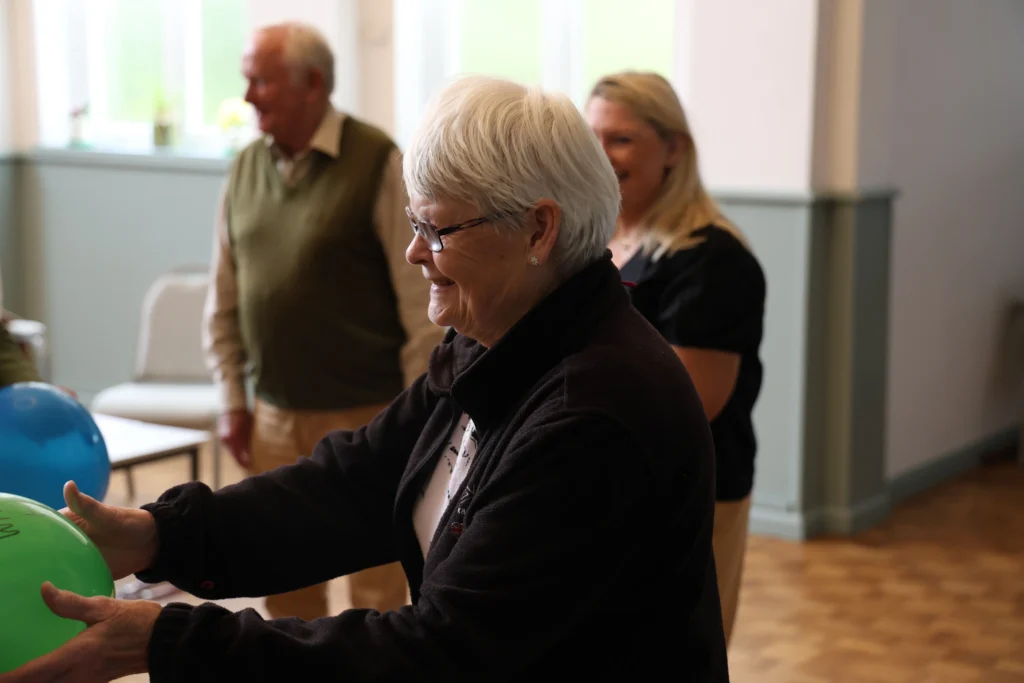 A woman with short grey hair smiling while holding a balloon during an activity at the Family Dementia Workshop.