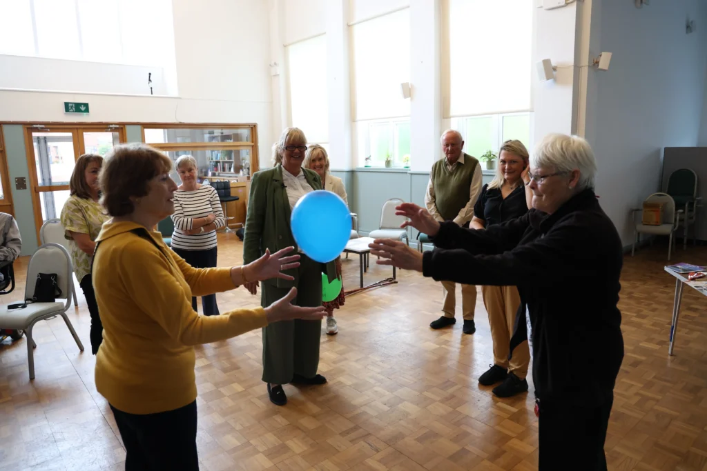 A woman in a yellow sweater passing a balloon to another woman during a group activity at the Family Dementia Workshop.