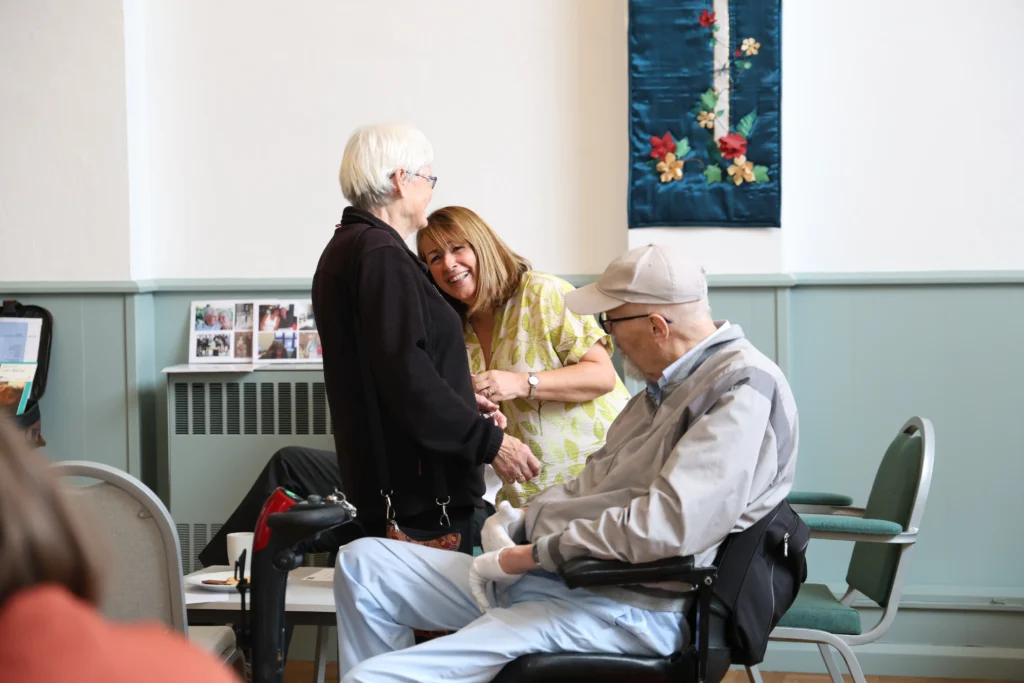 A group of people interacting warmly at the Family Dementia Workshop, with one woman hugging another.