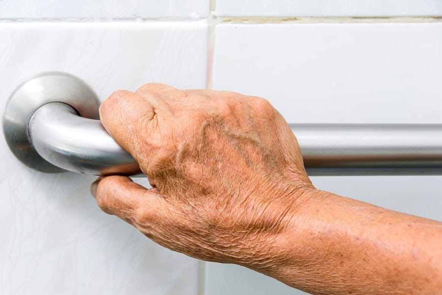 An older person's hand holding onto a grab rail in the bathroom