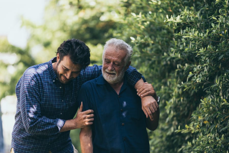 An younger man with his arm around an older man, both laughing warmly while walking 