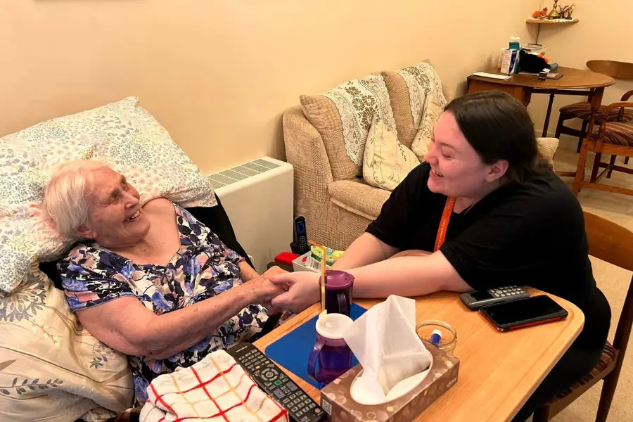 Caregiver, Emma and her client sat smiling at eachother while holding hands