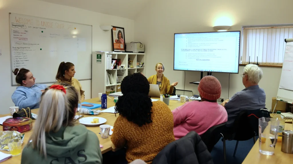 A group of caregivers attending a training session, with learning and development manager, Jo Cleary, presenting information on a large screen at the front of the room