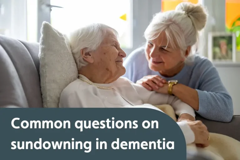 "An elderly woman sitting comfortably on a couch, smiling at her caregiver who leans in, offering comfort and support. The overlay text reads: 'Common questions on sundowning in dementia,'